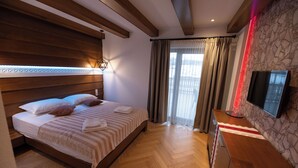 A hotel room with a wooden bed, a flat-screen TV, and a stone-patterned wall. - Casa Danciu Fanate – Tradiție, liniște și ospitalitate în inima naturii (Cernești)
