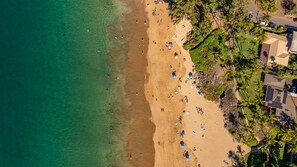 Ein Luftbild von einem Strand mit Menschen, Sonnenschirmen und Palmen.