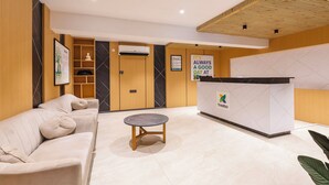 A reception area with a reception desk, a sofa, a small round table, and a bulletin board. - Treebo Premium Taara (Chennai)