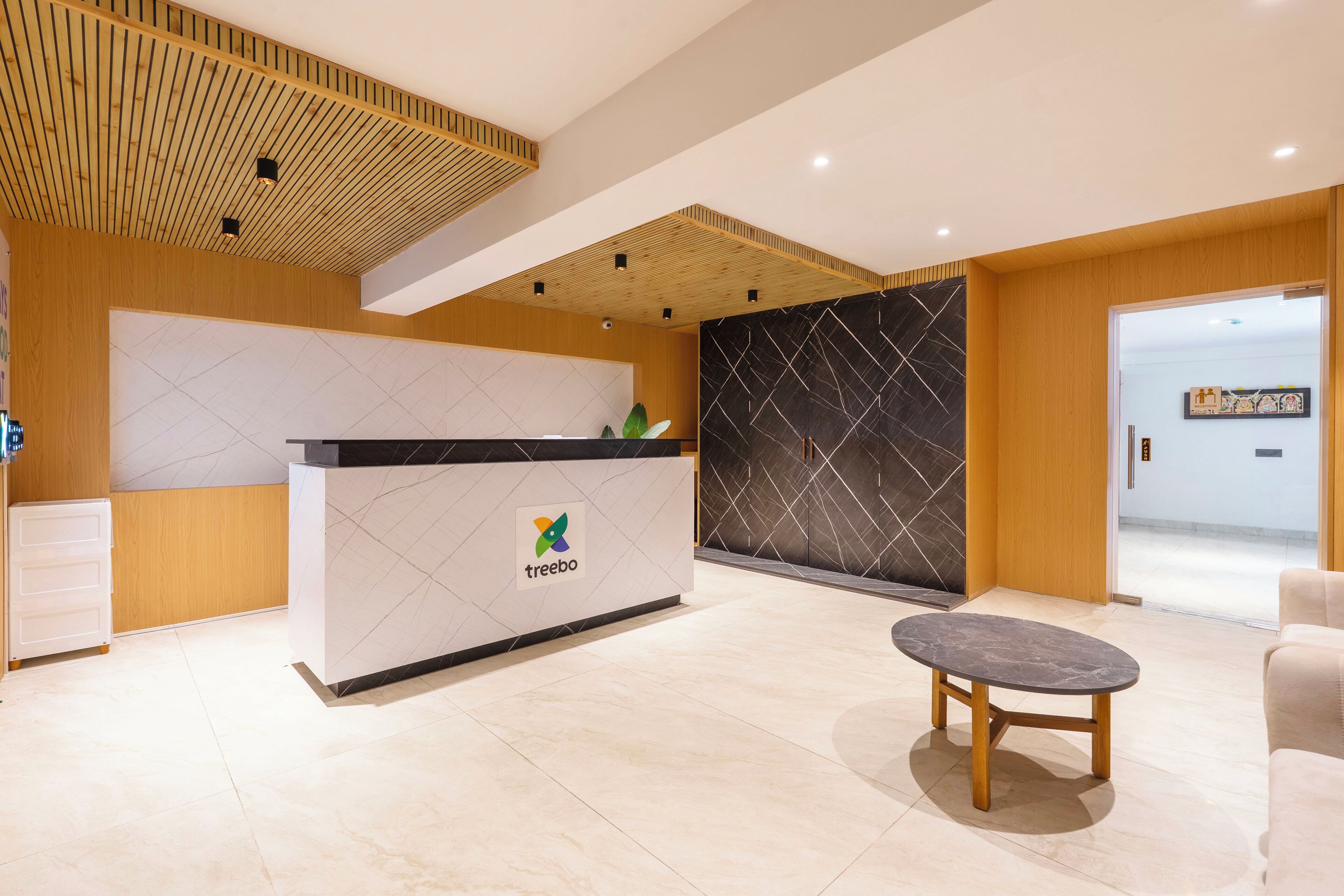 Un área de recepción con un mostrador de madera, suelo de baldosas de mármol y un diseño moderno con un patrón geométrico en la pared.
