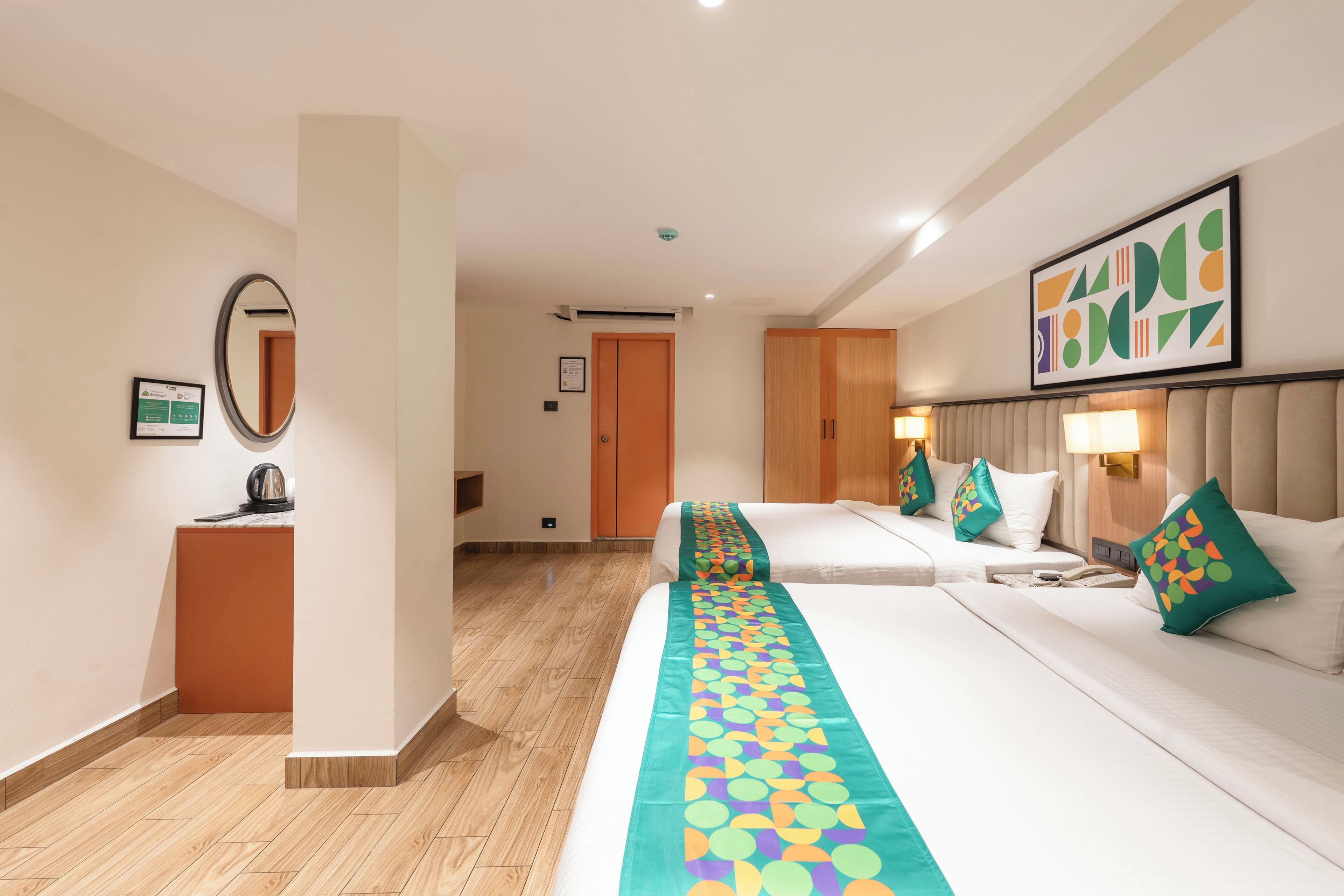 Hotellihuone, jossa on kaksi sänkyä, suuri peili, puinen työpöytä ja värikäs pöytäliina.
