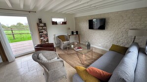 Een woonkamer met een grijze bank, een rieten fauteuil en een boekenkast.