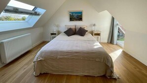Een slaapkamer met dakraam, een bed met kussens, een nachtkastje met lamp en een schilderij aan de muur.