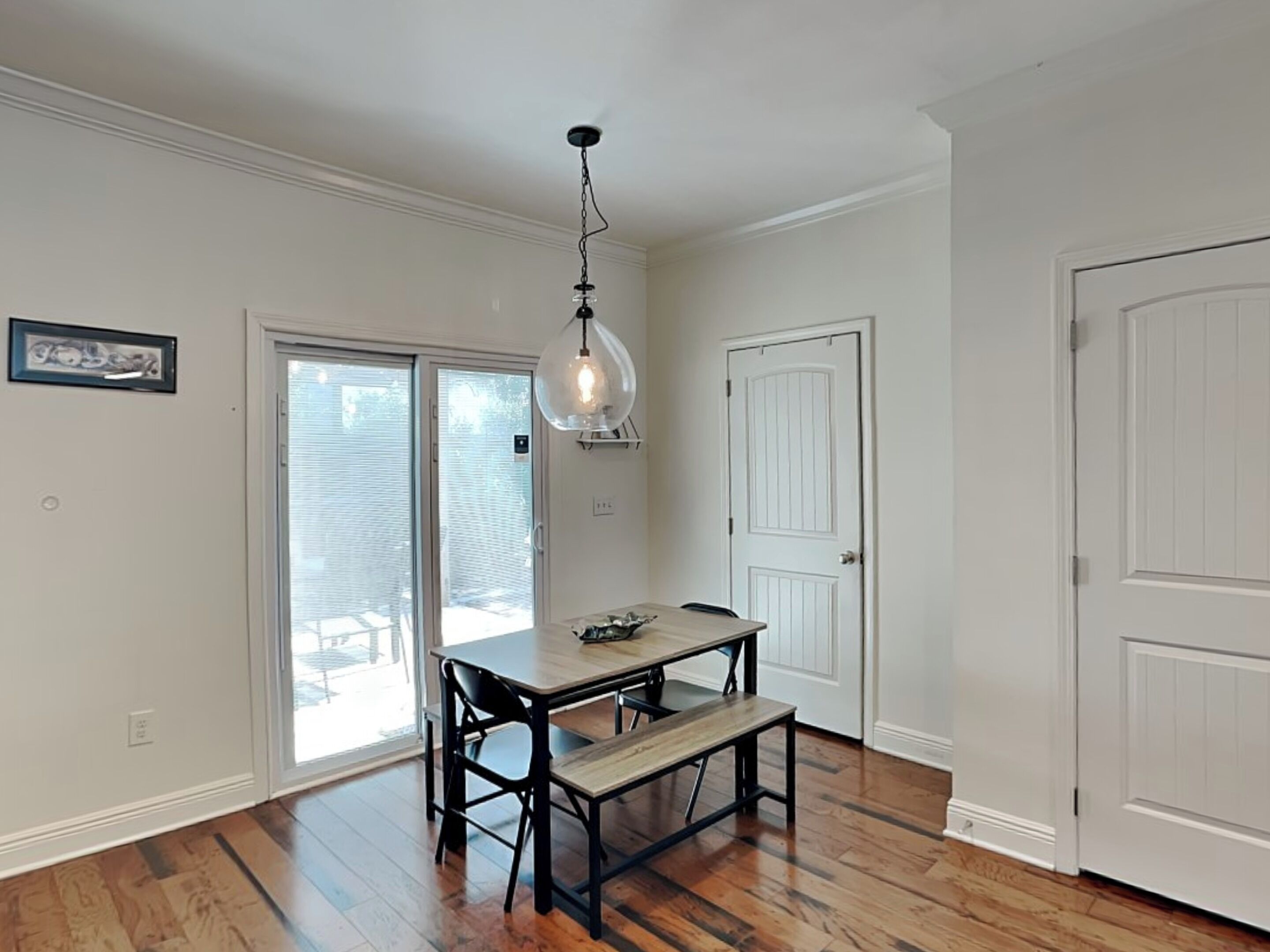 Un comedor con mesa y sillas de madera, una lámpara colgante y un ventanal corredero que da al exterior.