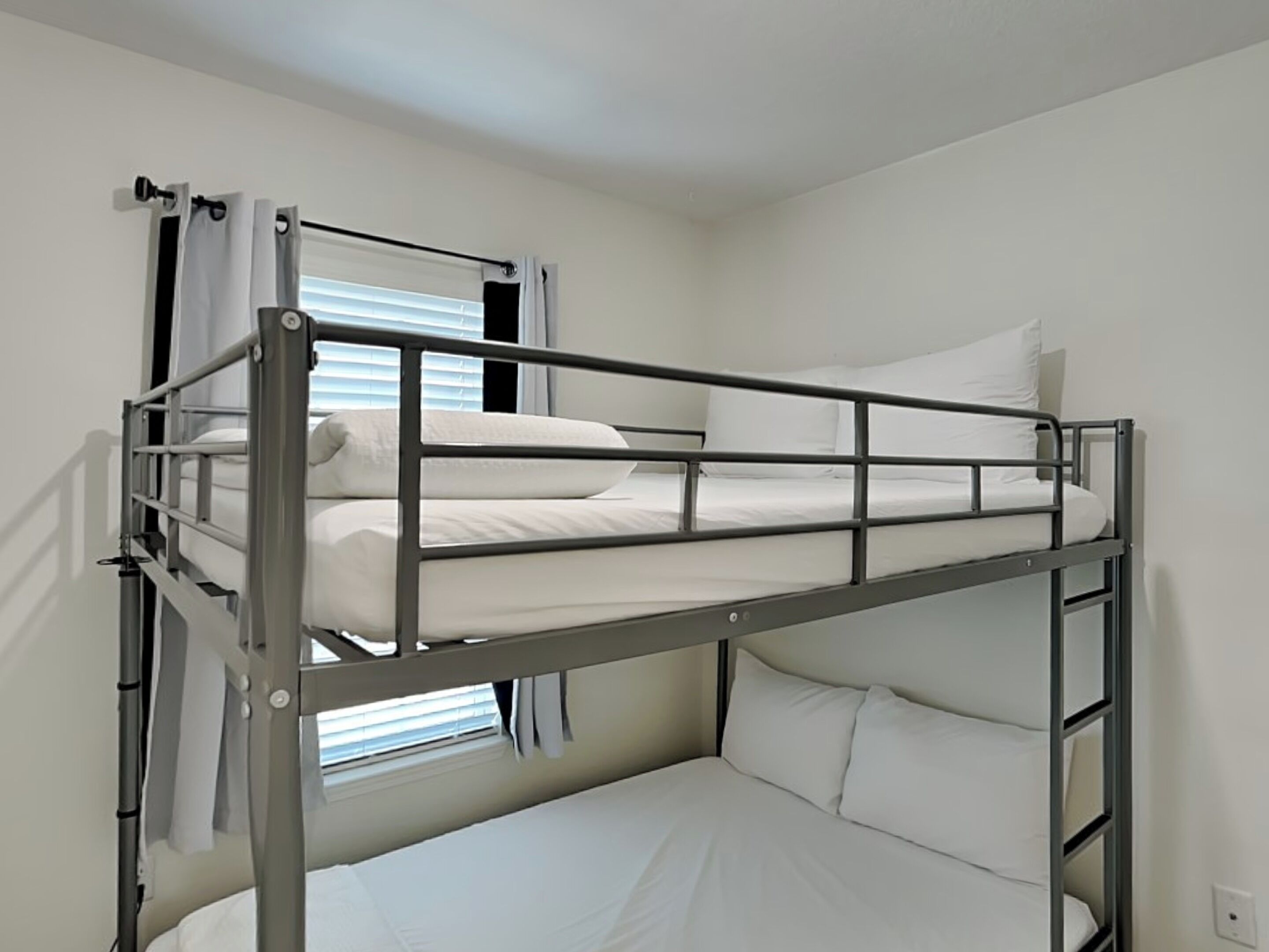 A bunk bed room with white bedding and a window with blinds.