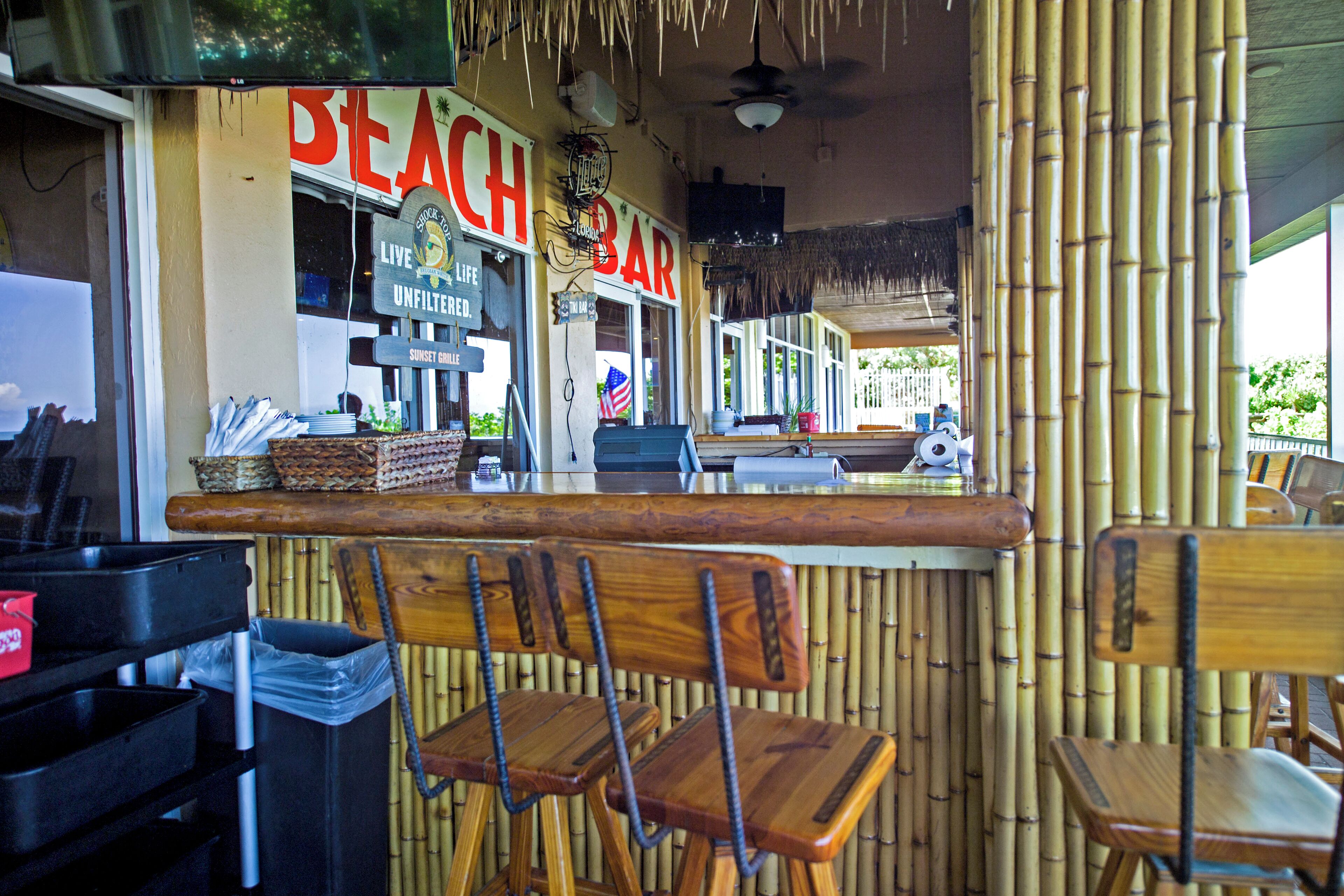 A beach bar with wooden chairs and a bamboo wall.