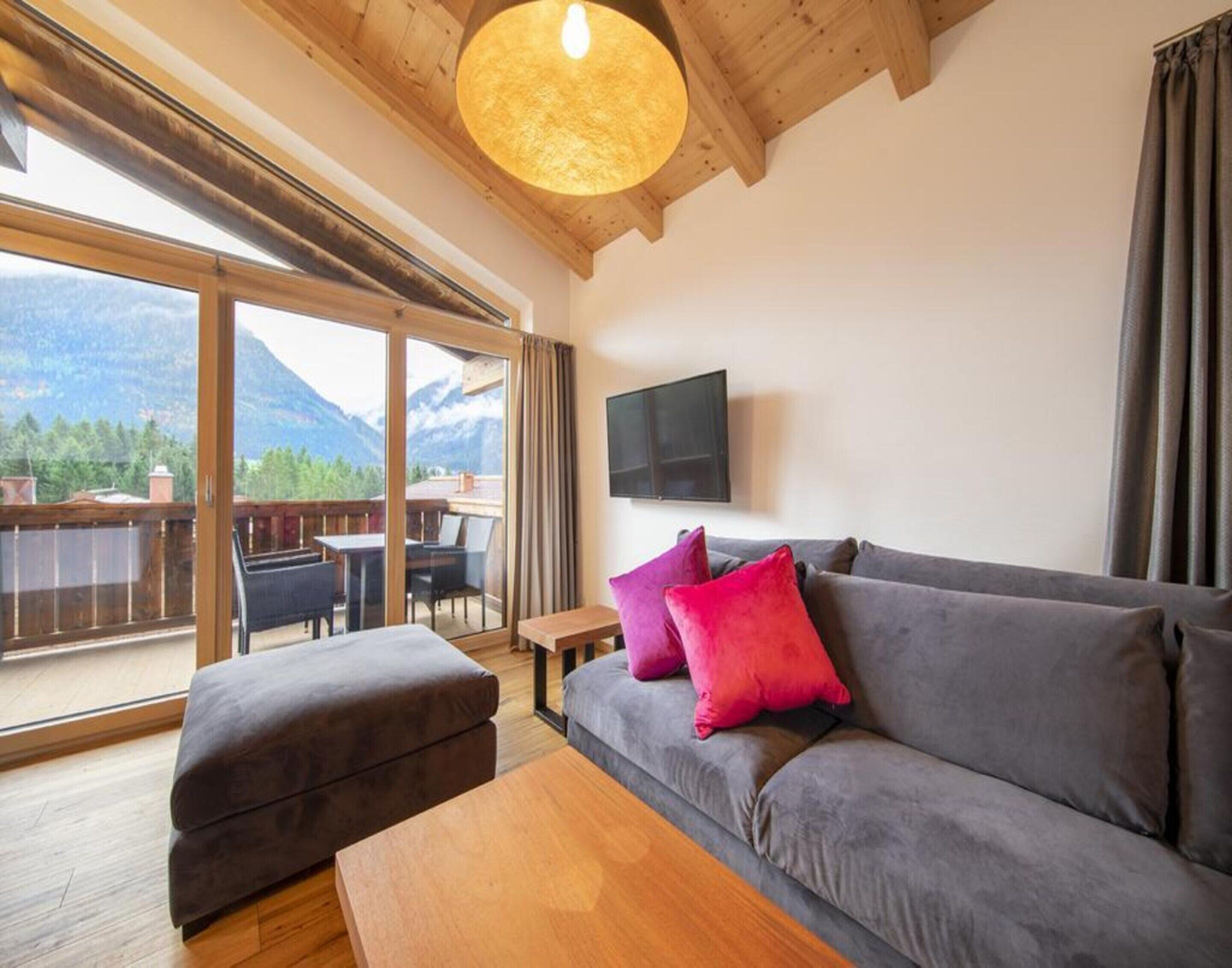 A modern living room with a grey sofa, a wooden coffee table, and a TV mounted on the wall.