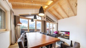 A spacious dining area with a long wooden table and modern chairs, large windows offering mountain views, and a high wooden ceiling. - Stylish Alpine Chalet With Carport (Neukirchen am Grossvenediger)