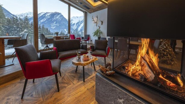A modern living room with a fireplace, large windows, and a view of snow-capped mountains. - Stylish Alpine Chalet With Carport (Neukirchen am Grossvenediger)