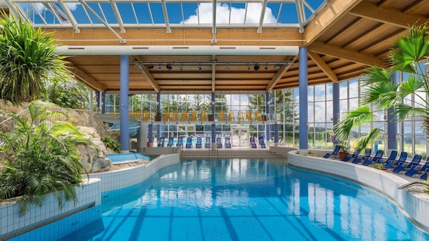 An indoor swimming pool with clear blue water, surrounded by lounge chairs and potted plants.