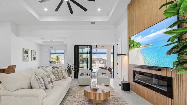 A modern living room with a large flat-screen TV, a beige sofa, and a coffee table. - Luxury Waterfront Retreat! Hot Tub and Heated Pool. (Cape Coral)