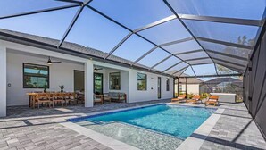 A covered swimming pool area with a patio, seating, and a view of the outdoors. - Luxury Waterfront Retreat! Hot Tub and Heated Pool. (Cape Coral)