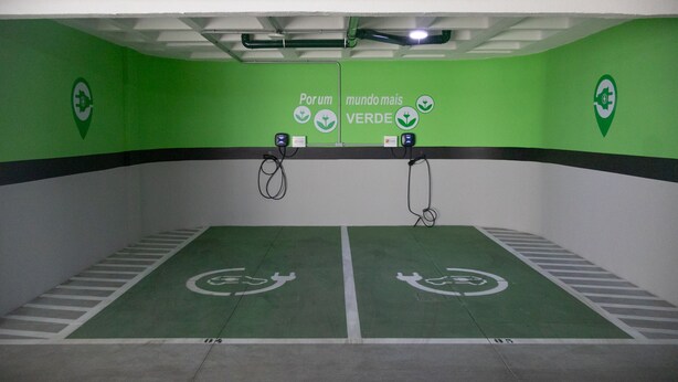 Un estacionamiento con paredes verdes y pisos blancos, que cuenta con parquímetros y flechas direccionales verdes.