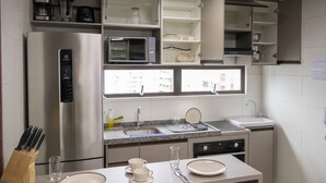 Eine moderne Küche mit einem Edelstahl-Kühlschrank, einer Mikrowelle und einem Geschirrspüler. Über der Arbeitsplatte befinden sich Schränke und über der Spüle ein Fenster.
