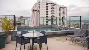 Un área de piscina en la azotea con barandilla de cristal, una mesa redonda y sillas.