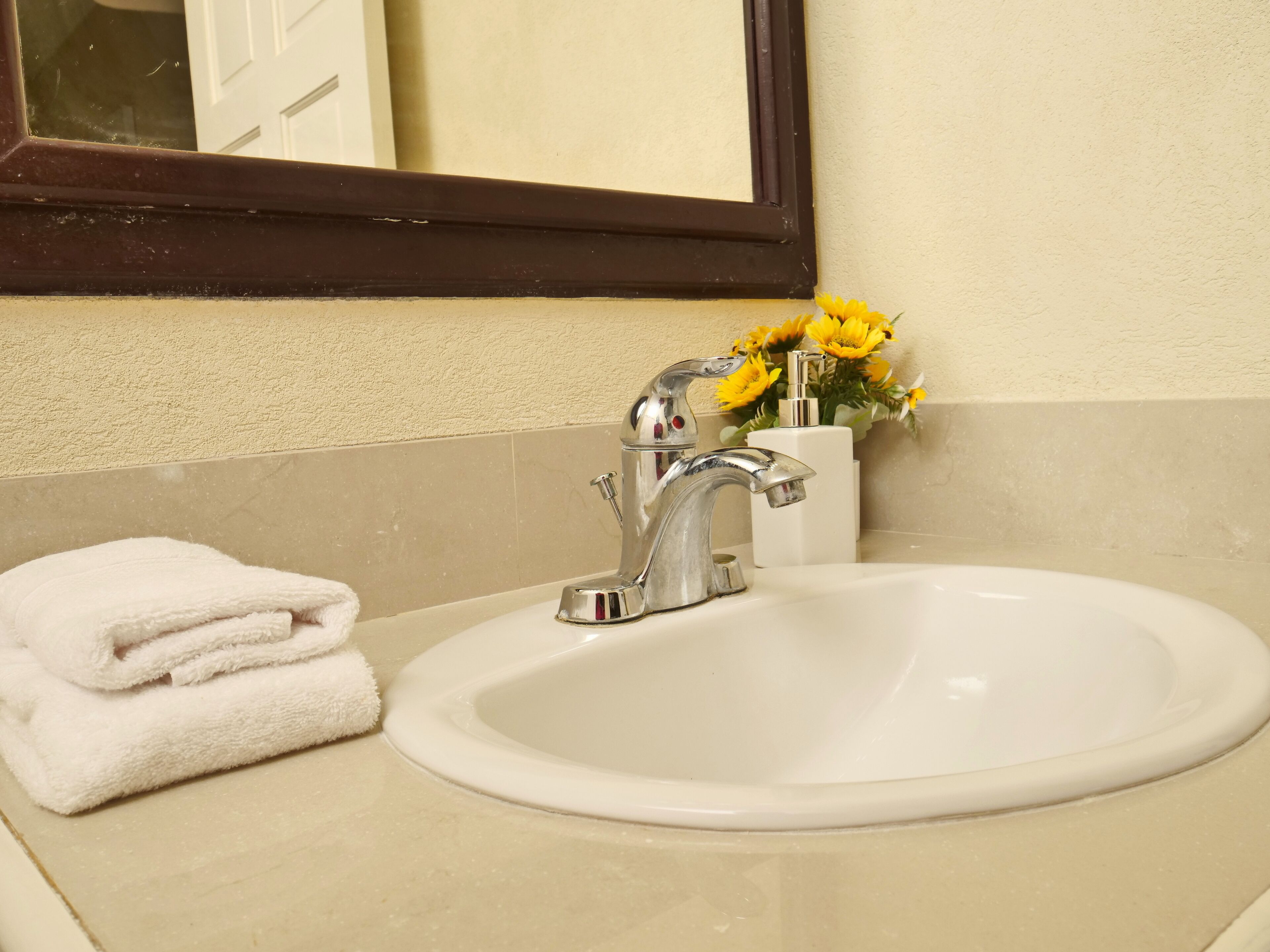 A bathroom sink with a mirror above it, a towel on the counter, and a vase with yellow flowers.