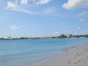 Une plage aux eaux calmes, avec un rivage sablonneux et des bâtiments qui se dressent au loin.