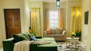 Una sala de estar con un sofá verde, un sofá beige, una mesita redonda y un tapete estampado.
