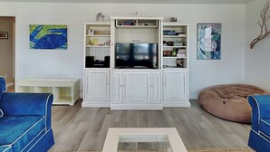 Una sala de estar con un mueble blanco para entretenimiento, dos sofás azules, un sillón de peluche y una mesa de centro.
