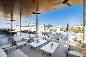 A rooftop lounge with outdoor seating, ceiling fans, and a view of the city.