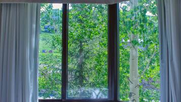 A room with a large window overlooking a green landscape with trees and a building in the distance.