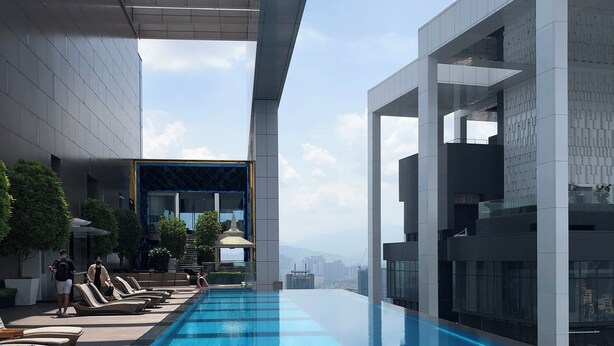 Piscina infinita no terraço com espreguiçadeiras, área de estar coberta e vista para o horizonte da cidade.