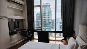 Quarto de hotel com cama, escrivaninha, cadeira, televisão e vista para um edifício com a inscrição 'SUNWAY'.