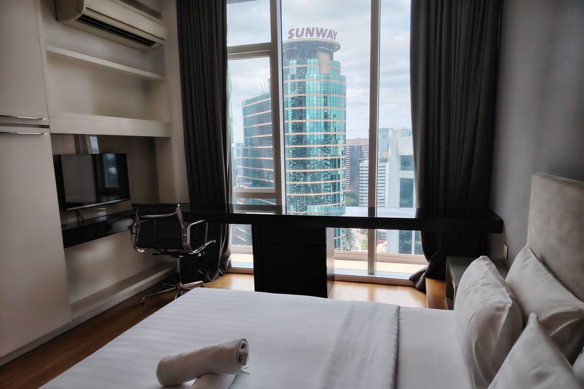 Een hotelkamer met een bed, een bureau, een stoel, een televisie en uitzicht op een gebouw met 'SUNWAY' erop.