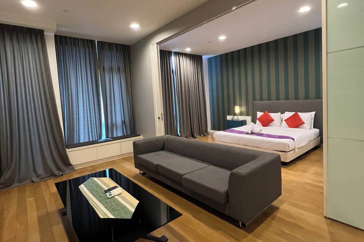 Een moderne hotelkamer met een grijze bank, een klein tafeltje met een tijdschrift, een bed met rood-witte beddengoed en een gestreepte wand.