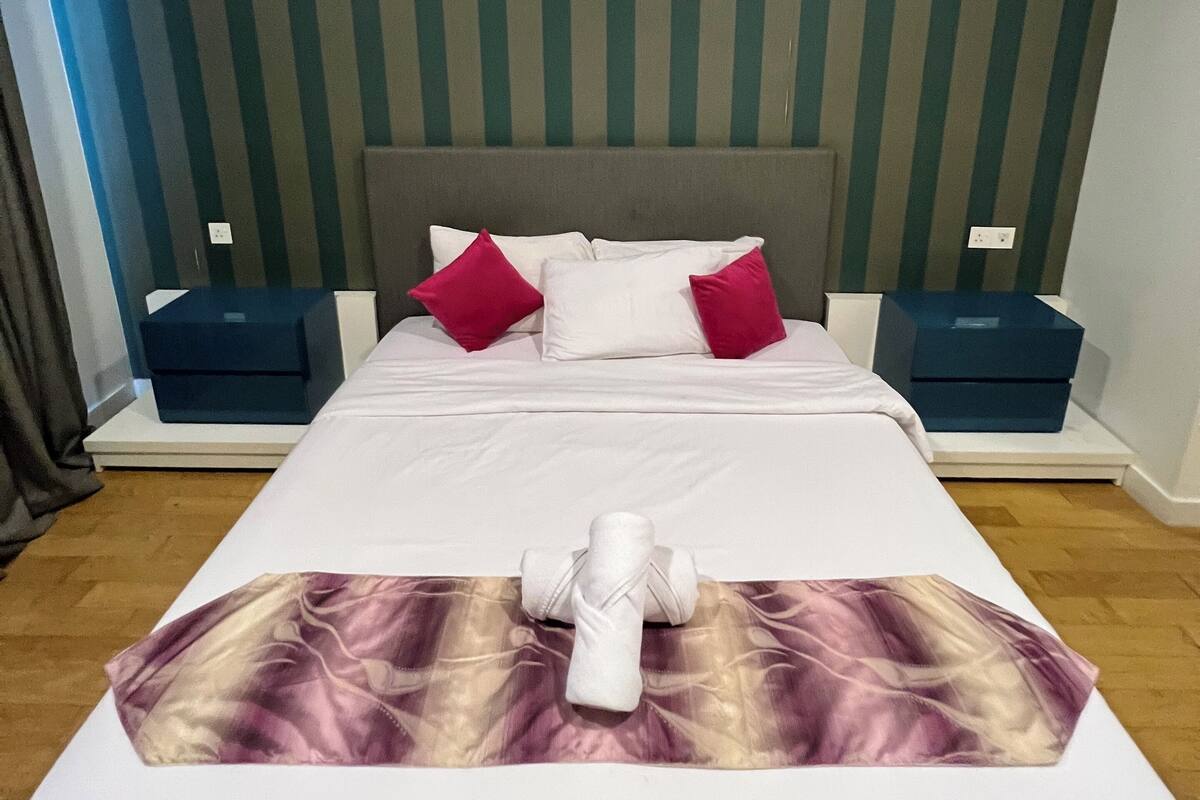 Een hotelkamer met een bed, kussens, nachtkastjes en een gestreepte wand.
