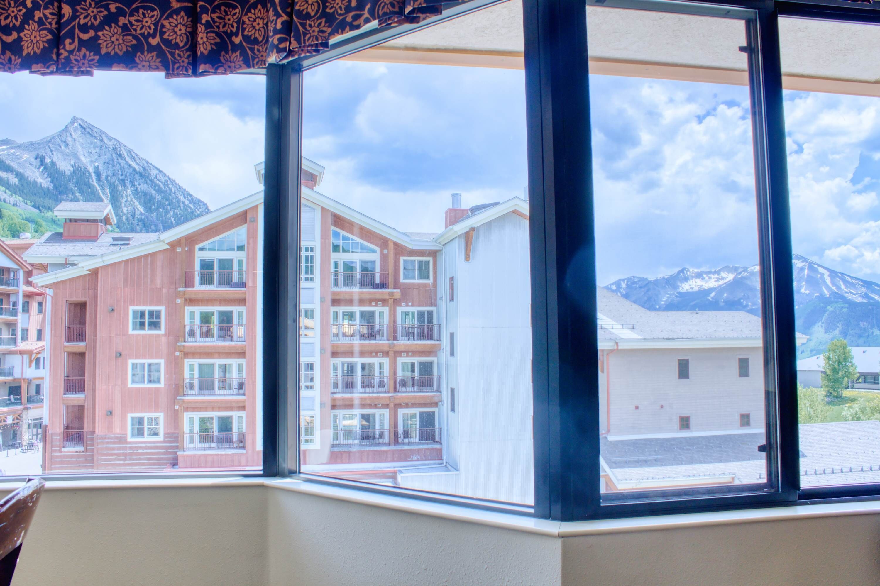 Une chambre d’hôtel dotée d’une grande fenêtre donnant sur une montagne et les bâtiments avoisinants.