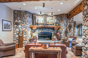 A stone-walled room with a fireplace, leather seating, and a wooden table. - Studio with Pool, Hot Tub, Biking Trails, Pets Okay (Crested Butte)