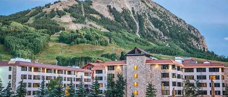 A multi-story hotel with a stone facade, surrounded by a mountainous landscape.