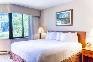 A hotel room with a large bed, a window with curtains, a bedside lamp, and a framed picture on the wall. - Studio with Pool, Hot Tub, Biking Trails, Pets Okay (Crested Butte)