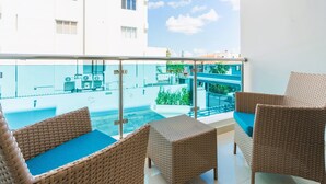 Ein Balkon mit Korbmöbeln und Blick auf einen Swimmingpool und Gebäude.