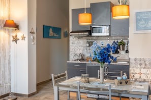 Eine moderne Küche mit grauen Schränken, einer Mikrowelle und einer gefliesten Spritzschutzwand. Es gibt einen Esstisch mit Stühlen und eine Vase mit blauen Blumen.