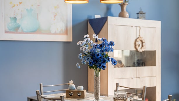 Una mesa de comedor con sillas, un jarrón de flores azules y un aparador al fondo.
