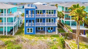 A multi-story building with balconies, a front porch, and a fenced backyard.