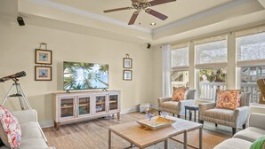 A spacious living room with a ceiling fan, large windows, a TV, and a cabinet.