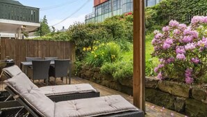 Eine Terrasse mit Korlounge-Stühlen und einem Tisch, umgeben von einem Garten mit verschiedenen Pflanzen und Blumen.