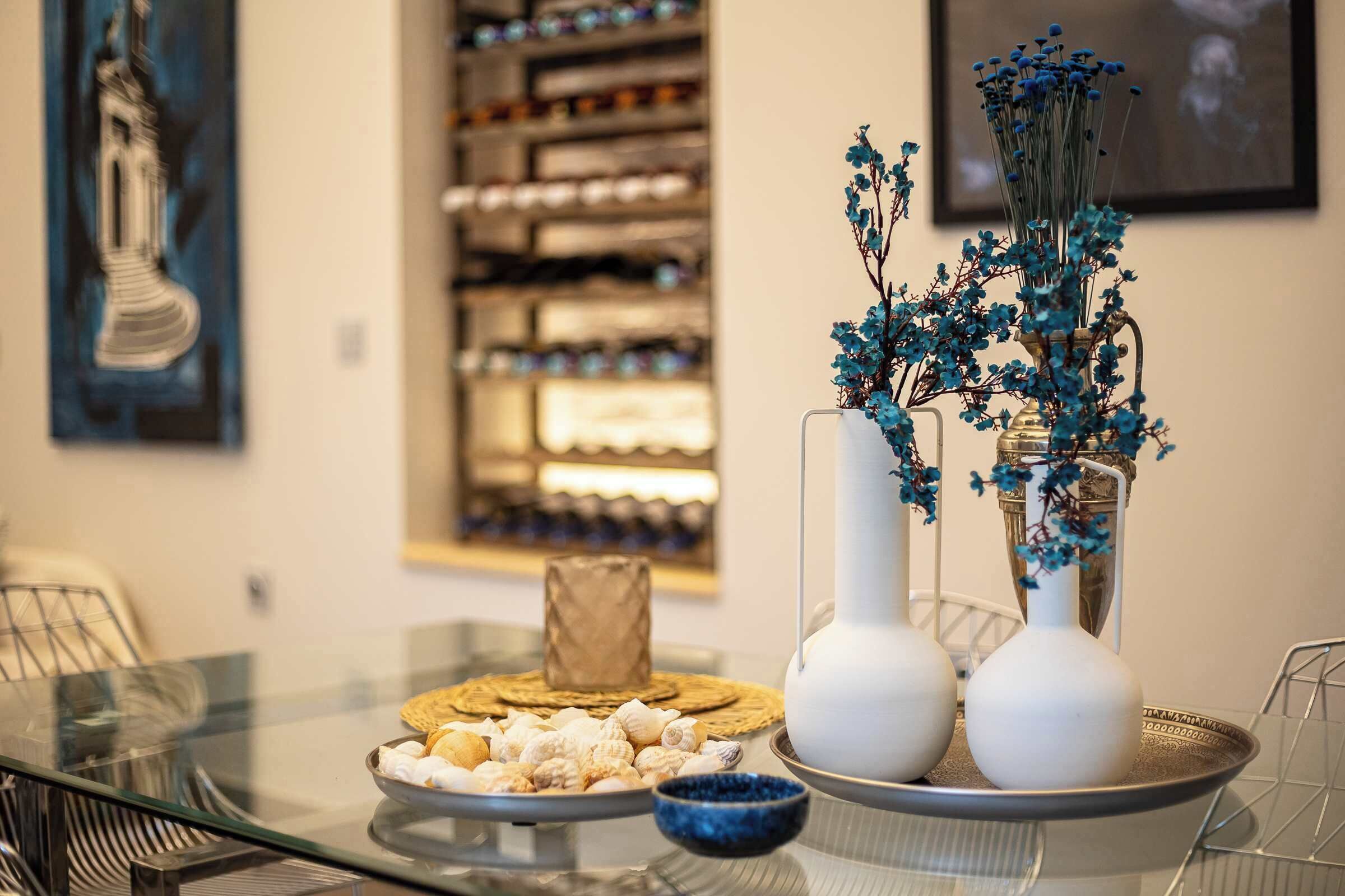 Una mesa de comedor con un plato de galletas, un tazón pequeño y dos jarrones con flores azules.
