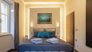 Een keurig opgemaakt slaapkamer met een groot bed, een gestoffeerd hoofdeinde, een schilderij aan de muur en een raam met gordijnen.