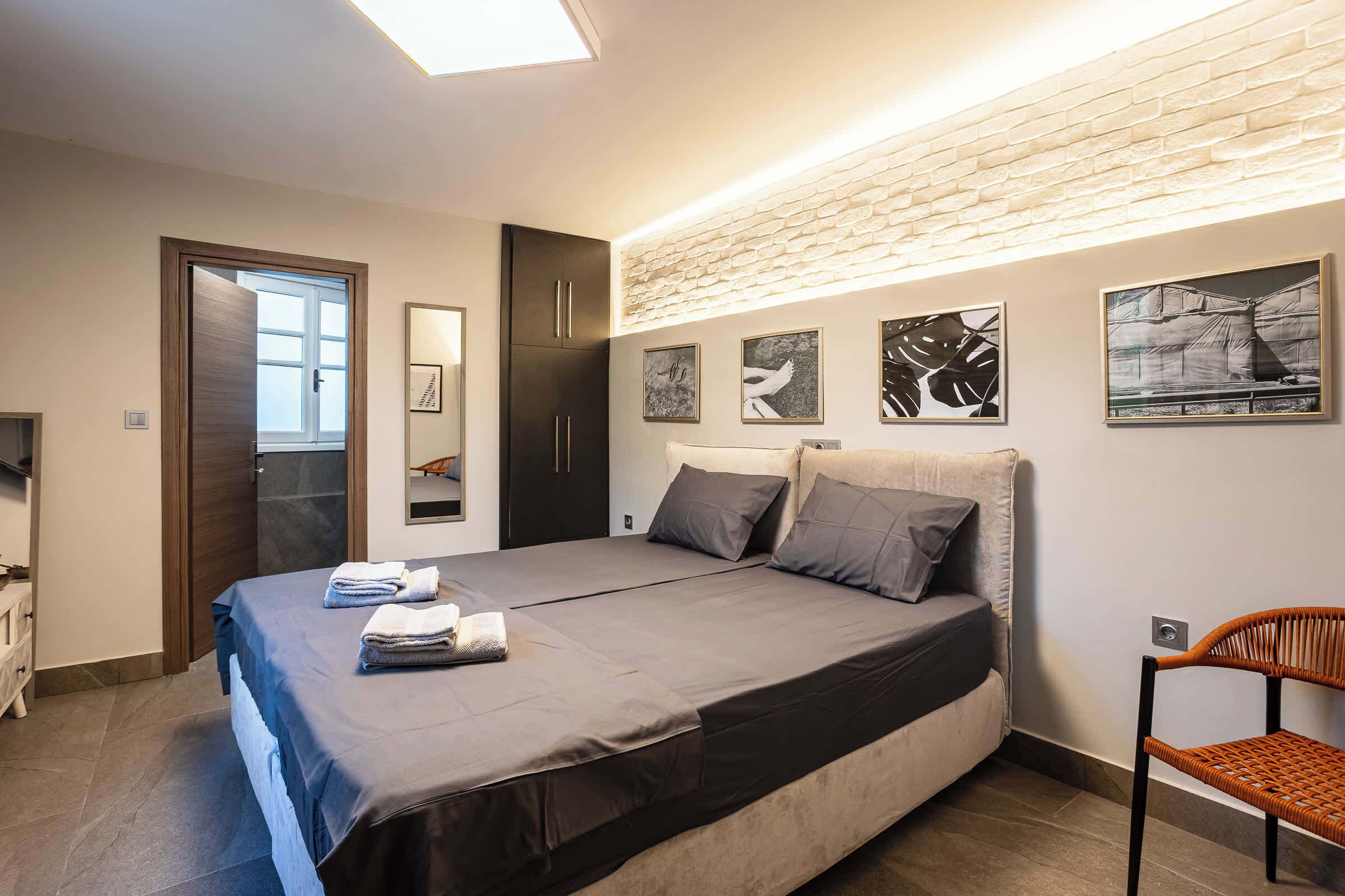 Un dormitorio con cama, una silla, armario y cuadros en la pared.