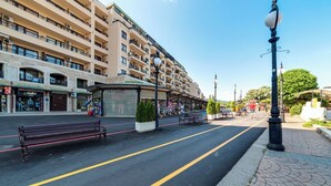 A street with a bench, a kiosk, and a building with balconies.