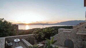 A stone terrace with a table and chairs, overlooking a body of water and mountains. - Niki's Tower - Exclusive Serene Seaview Stone Gem (Kalamata)