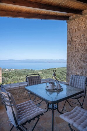 Una terrazza esterna con tavolo e sedie, vista sul mare e un muro in pietra.