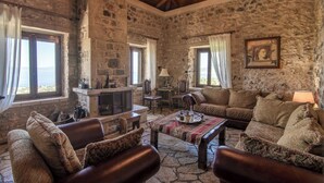 A stone-walled room with a fireplace, leather sofas, a coffee table, and a view of the sea. - Niki's Tower - Exclusive Serene Seaview Stone Gem (Kalamata)
