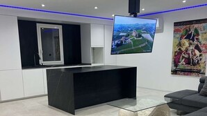 Una sala moderna con televisor de pantalla plana montado en la pared, un mueble de entretenimiento negro, un sofá gris y una escultura decorativa de piedra en el suelo.