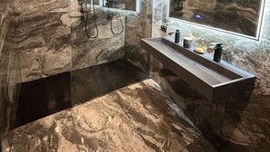 Un baño moderno con paredes de mármol, un espejo grande y un mueble de tocador elegante.