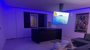 Una sala de estar moderna con un televisor de pantalla plana montado en la pared, un mueble de entretenimiento negro, una mesa de centro de vidrio y un sofá gris.
